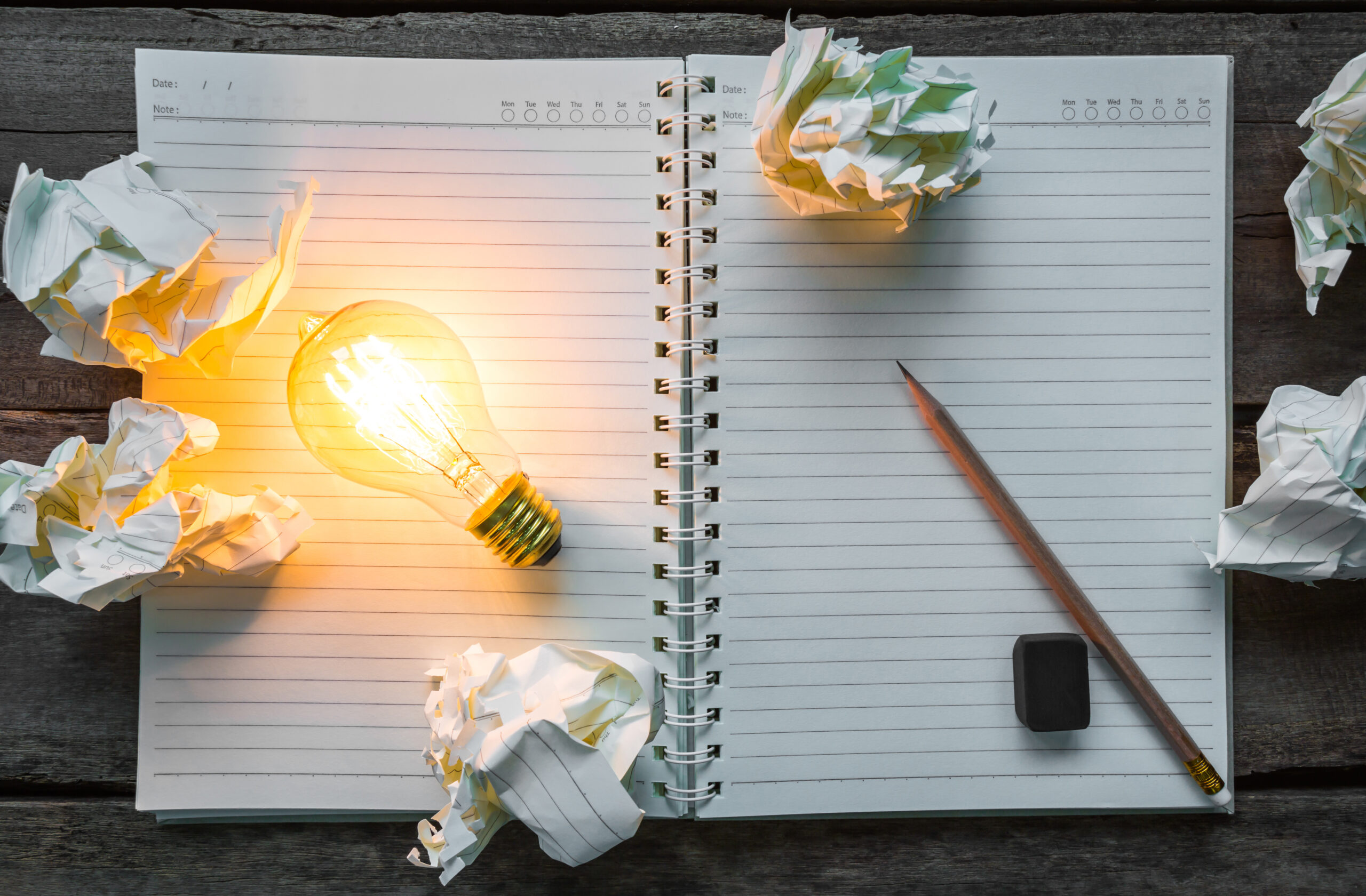 Zdjęcie przedstawiające zeszyt, ołówek i świecącą żarówkę.